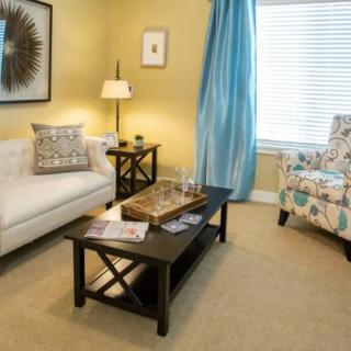 A cozy living room with a sofa, armchair, and coffee table, accented by wall art and bright blue curtains.