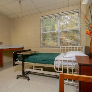 A clean and minimalist hospital patient room equipped with a bed, bedside table, and natural light from the window.