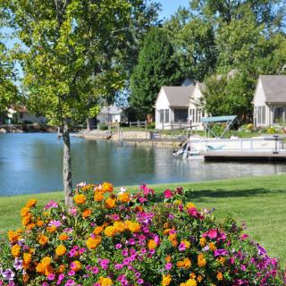 A scenic view of a lakeside area featuring vibrant flowers, cozy houses, and a serene dock.