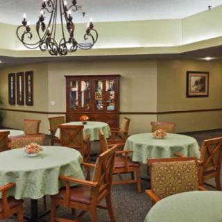 A well-appointed dining room with tables covered in light green tablecloths and wooden chairs, illuminated by an elegant chandelier.