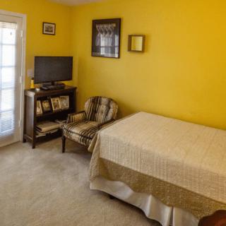 A cozy bedroom with yellow walls, featuring a bed, television, and chair.