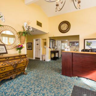 A warmly decorated lobby area featuring a wooden reception desk, patterned carpet, and elegant mirrors.