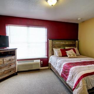 A cozy bedroom with a red accent wall, featuring a bed, dresser, and TV.