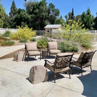 A cozy outdoor patio setup with cushioned chairs arranged around a central table, surrounded by lush greenery and a well-maintained backyard.