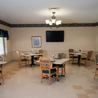 A well-lit dining area with several tables and chairs, featuring a television on the wall.