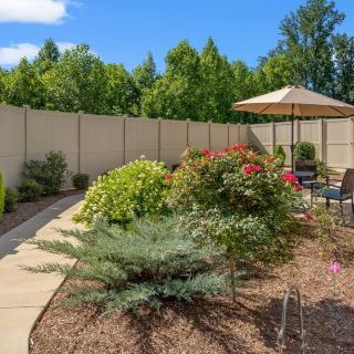 A beautifully landscaped backyard garden with a paved pathway, vibrant flowers, and outdoor seating under an umbrella.