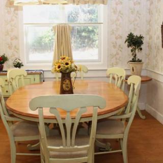 A cozy dining room with a round wooden table and chairs, decorated with a vase of sunflowers.