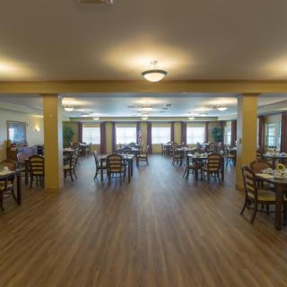 A spacious dining room with wooden floors, tables, and chairs arranged neatly under soft lighting.