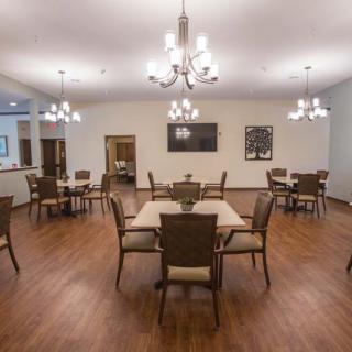 A spacious dining room with wooden floors, equipped with multiple tables and chairs, illuminated by elegant chandeliers.