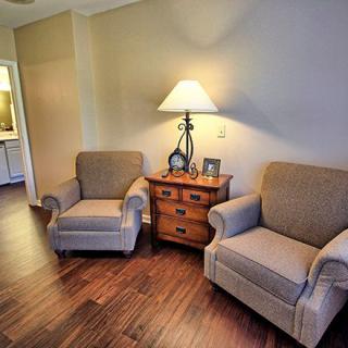 A cozy living room corner featuring two armchairs, a wooden side table, and a lamp on a wooden floor.