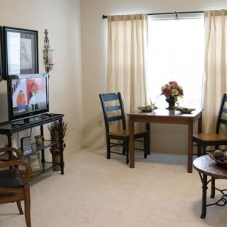 A cozy living room with a TV, chairs, and a table near a window.