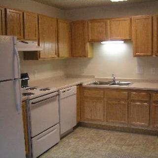 A simple kitchen with wooden cabinets, a refrigerator, stove, and sink.