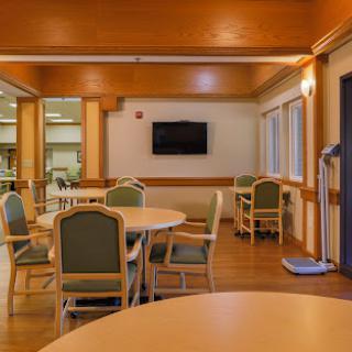 A spacious and well-lit dining area in a rehabilitation center, equipped with tables, chairs, and a television.