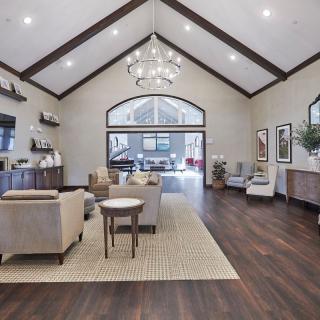 A spacious and modern living room with high ceilings, featuring elegant sofas and armchairs, a large chandelier, and wood flooring.