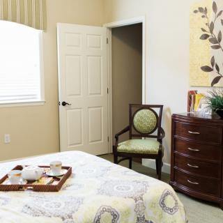 A cozy bedroom interior with a bed, chair, and dresser.