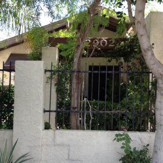 A cozy house surrounded by greenery and a wrought iron fence.