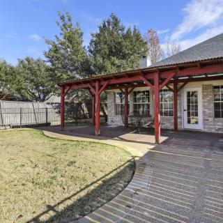 A backyard with a wooden deck and pergola next to a grassy lawn and trees.