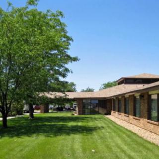 A brick building with a well-maintained lawn and trees under a clear blue sky.