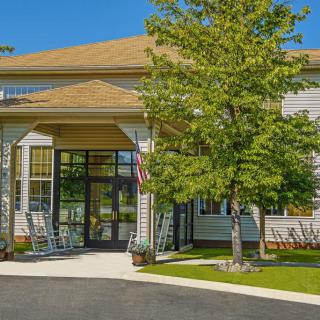 A suburban building entrance with a porch and rocking chairs, surrounded by greenery.