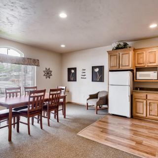 A well-lit dining area with a wooden table and chairs adjacent to a compact kitchen featuring a refrigerator and microwave.