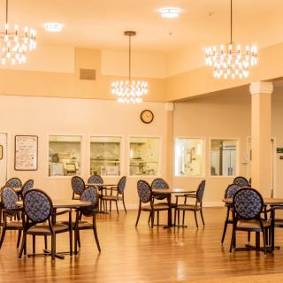 An elegant dining area with multiple tables and chairs, illuminated by chandeliers.