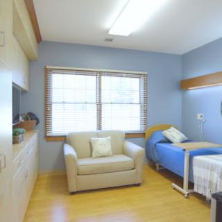 A well-lit hospital patient room featuring a bed, a sofa, and natural light from the windows.