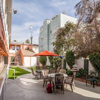 An outdoor patio area with tables, chairs, and umbrellas in an urban setting surrounded by buildings and trees.
