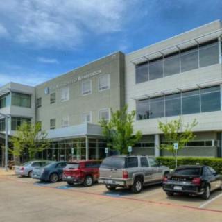 Modern office building with a parking lot and several parked cars on a clear day.