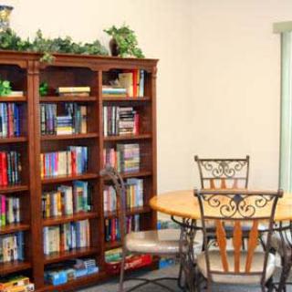A cozy library room featuring a wooden bookshelf filled with books and a round table with chairs.