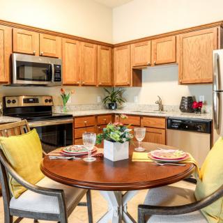 A modern kitchen with wooden cabinets, stainless steel appliances, and a cozy dining area featuring a round table with yellow-accented decor.