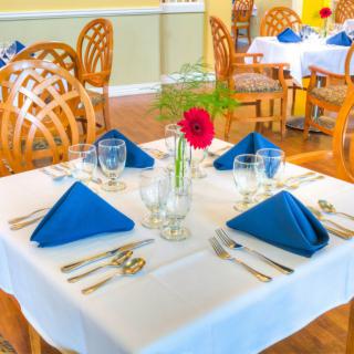 A well-set dining table in a restaurant with blue napkins and a floral centerpiece.
