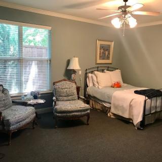 A cozy and well-lit bedroom featuring a single bed, armchairs, and natural light from the window.
