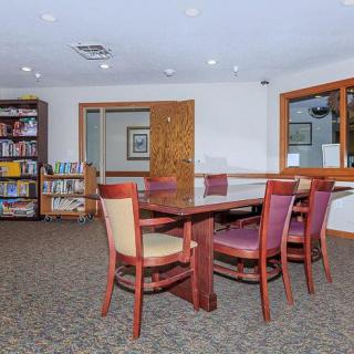 A cozy library space with a wooden table surrounded by chairs and shelves filled with books.