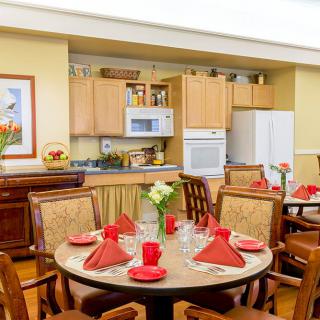 A cozy dining area with a round table set with red napkins and surrounded by wooden chairs, adjacent to a modern kitchen.