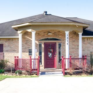 A brick house with a front porch featuring columns and a red door.