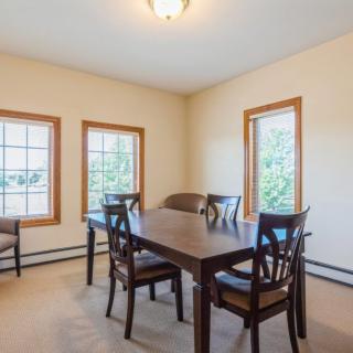 A cozy dining room with a wooden table, surrounded by four chairs and natural light coming through the windows.