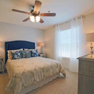 A cozy bedroom with a neatly made bed, ceiling fan, and soft lighting.
