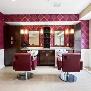 A modern hair salon interior with stylish red chairs and decorative wallpaper.