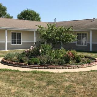 A beautifully landscaped garden featuring a circular flower bed and a central tree, set in front of a residential home.