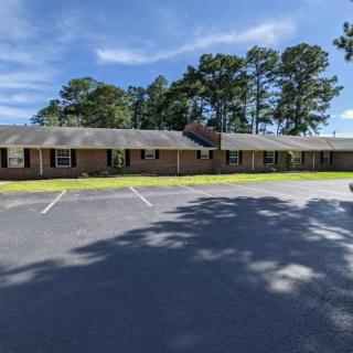 A single-story motel with a parking lot and surrounding trees under a clear blue sky.
