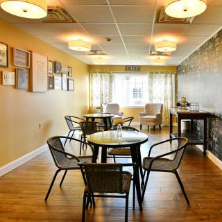 A cozy room with tables and chairs, featuring warm lighting and wooden floors.