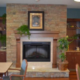 A cozy living room with a brick fireplace, surrounded by plants and wooden furniture.