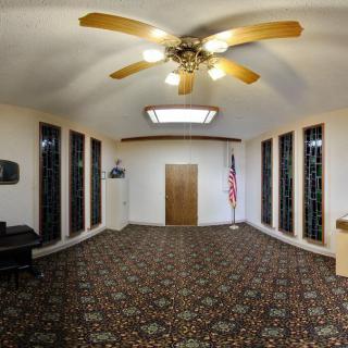 An empty room with a carpeted floor, ceiling fan, and an American flag beside stained glass windows.