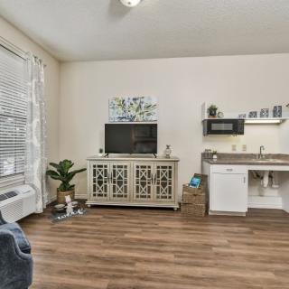 A cozy living space featuring a kitchenette, TV stand, and hardwood flooring.