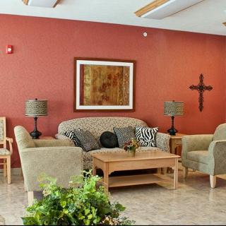 A cozy living room with a sofa and armchairs arranged around a wooden coffee table, complemented by wall art, a cross decoration, and green indoor plants.