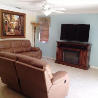 A cozy living room with brown sofas facing a TV on a fireplace stand, complemented by a painting and lamp.