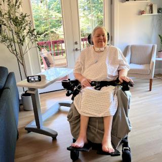 An elderly woman sitting in a wheelchair in a bright and cozy living room.