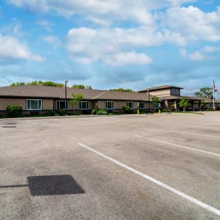 An empty parking lot in front of a low, elongated building under a partly cloudy sky.