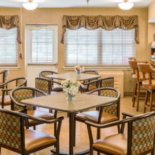 A cozy dining area with multiple tables and chairs, well-lit by natural light from the windows.