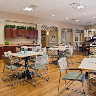 A cozy dining area with neatly arranged tables and chairs, featuring a kitchenette in the background.